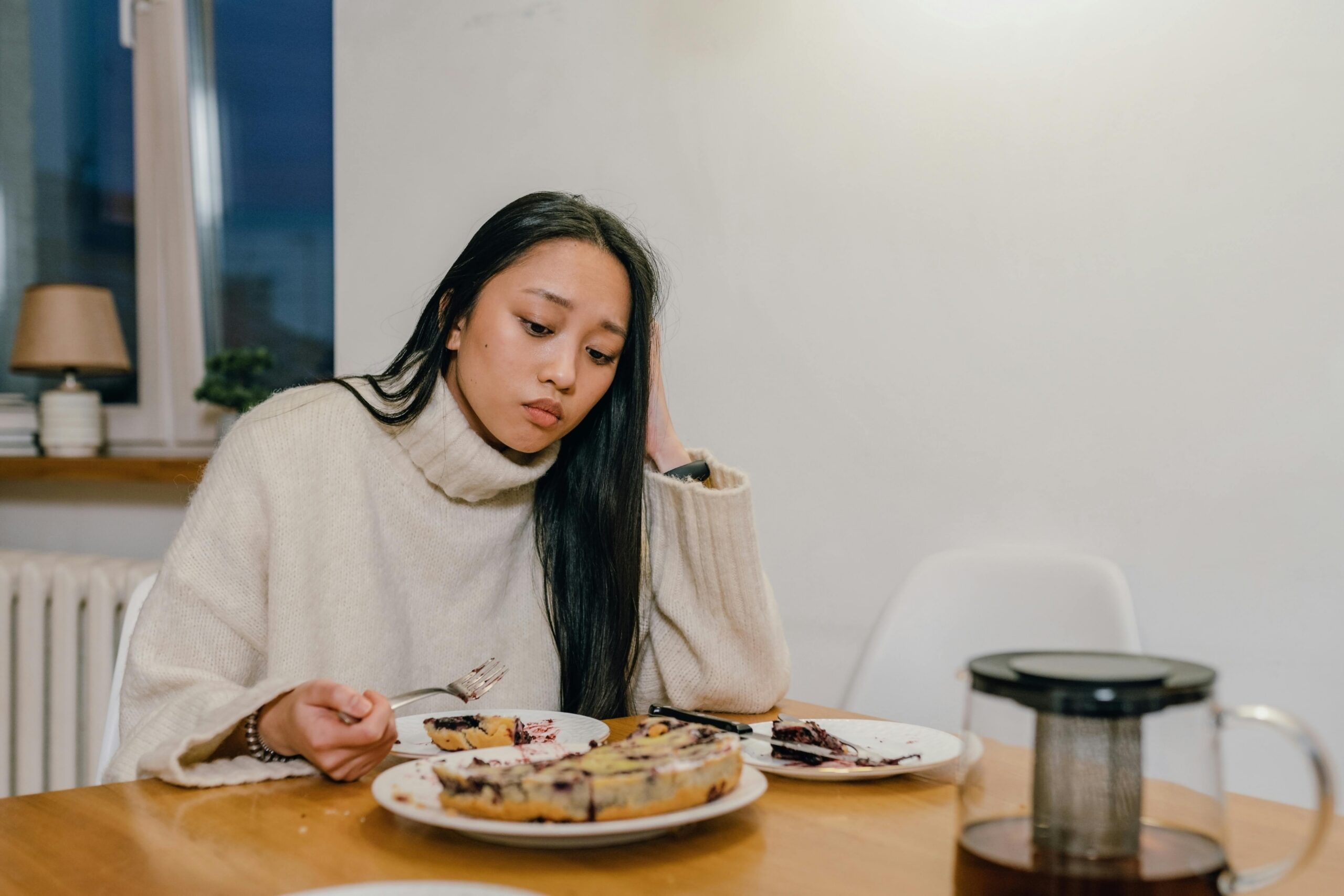 Woman sitting alone at a table looking distressed and disconnected from her food illustrating food anxiety