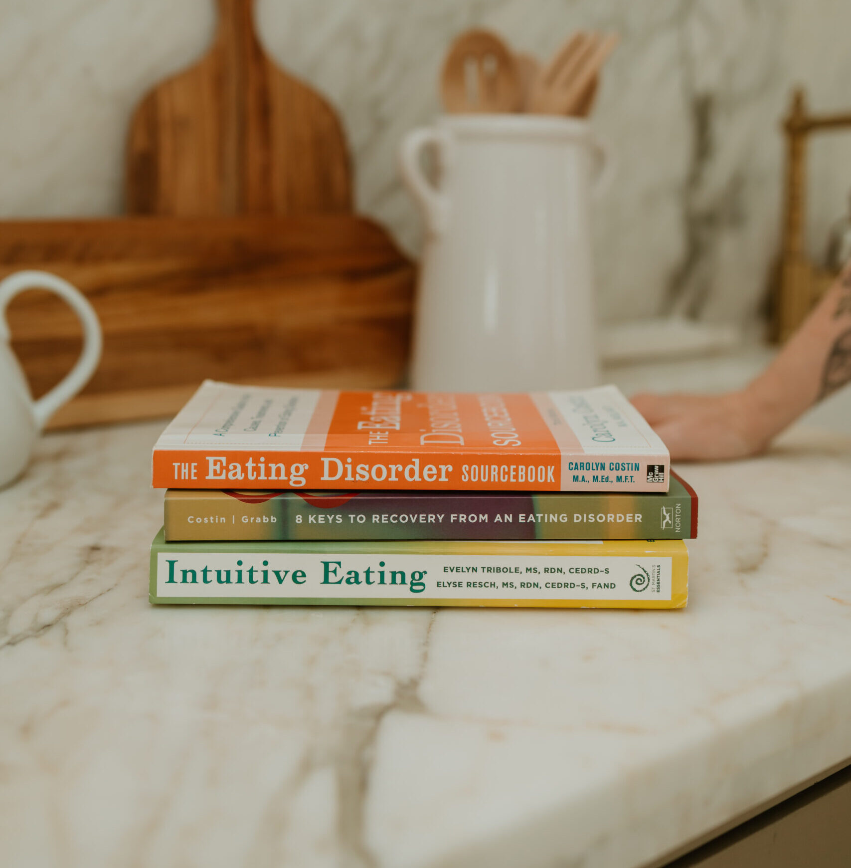Stack of eating disorder recovery books on a marble countertop at a Houston eating disorder therapy practice